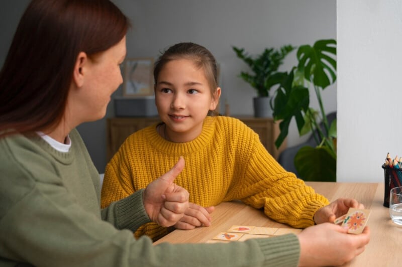 Mother and a daughter sit at a table, engaged in a thoughtful conversation